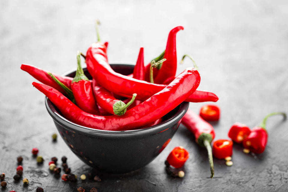 A black bowl filled with fresh red chili peppers against a gray background.