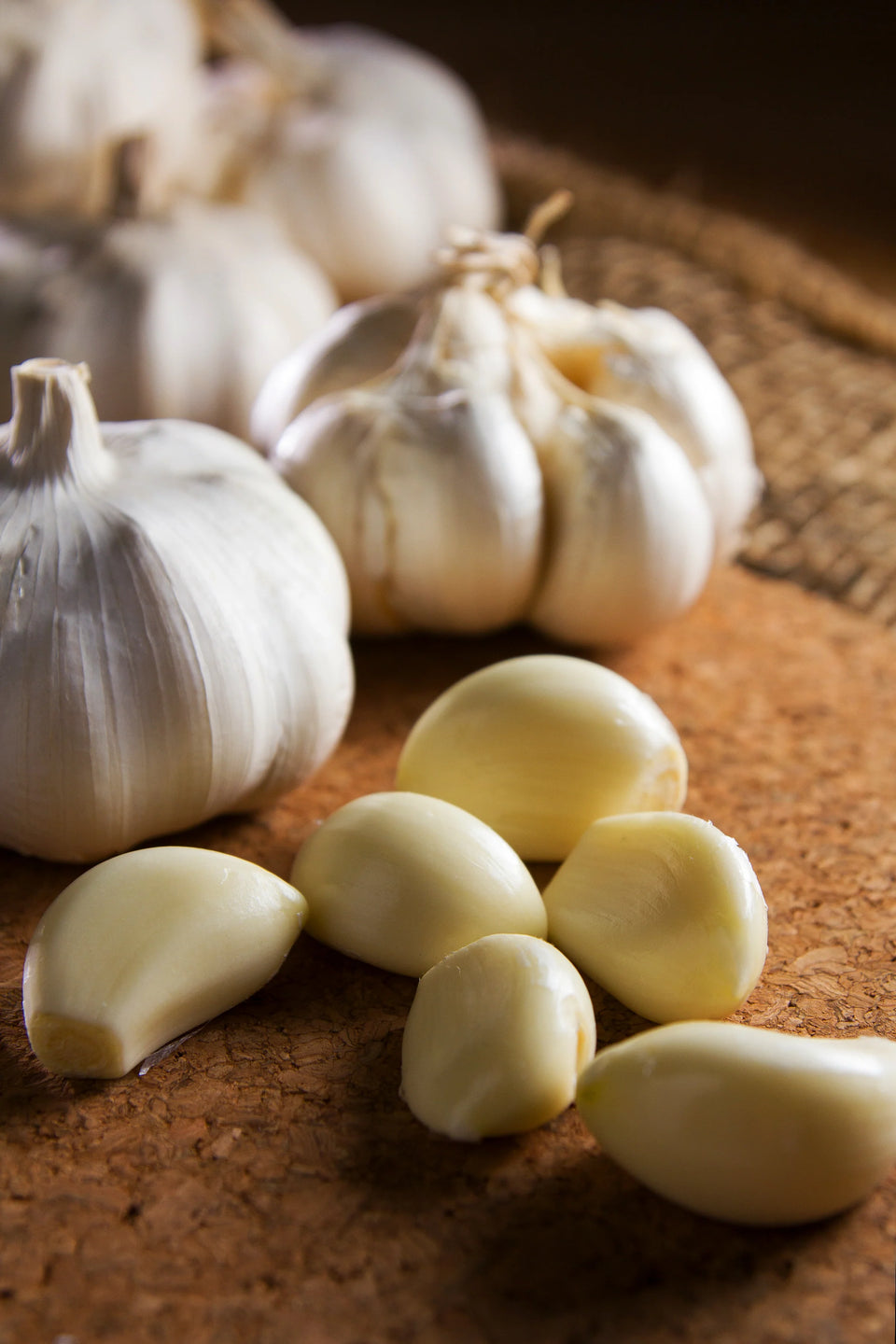 Whole garlic bulbs and peeled garlic cloves on a wooden surface.