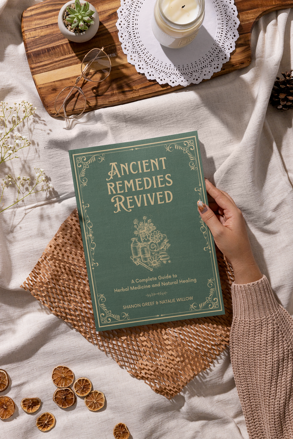 A person holding a book titled 'Ancient Remedies Revived' among cozy home decor items.